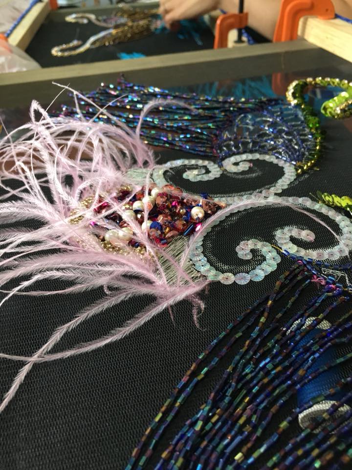 Materiales de bordado: plumas, hilos y mostacilla dispuestos sobre tela