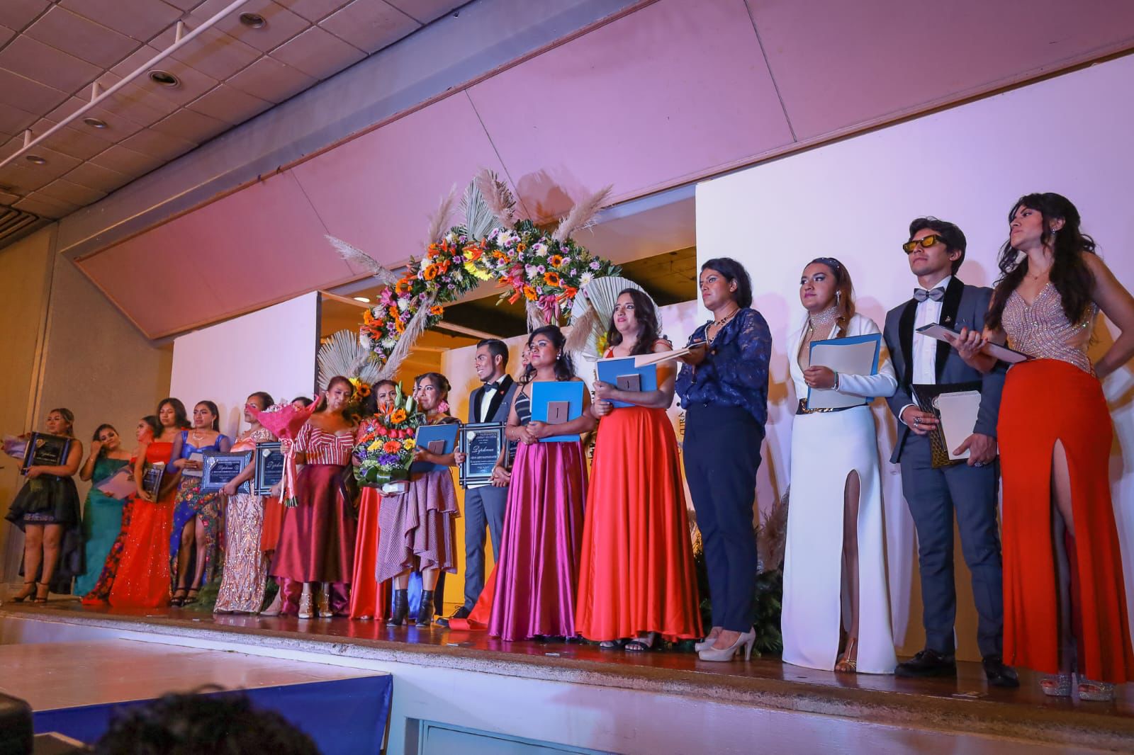 Grupo de egresadas en la pasarela con vestidos de noche de colores