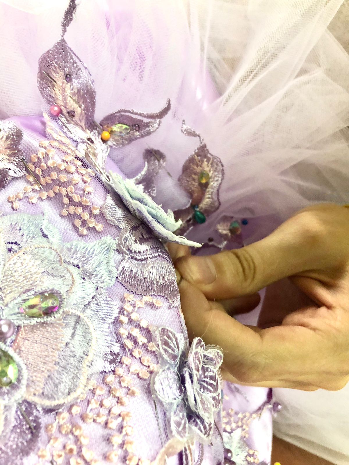Manos bordando perlas y cristales sobre organza lila